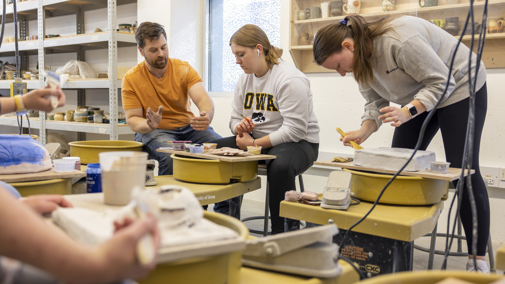 ceramics class with instructor working with student at a wheel